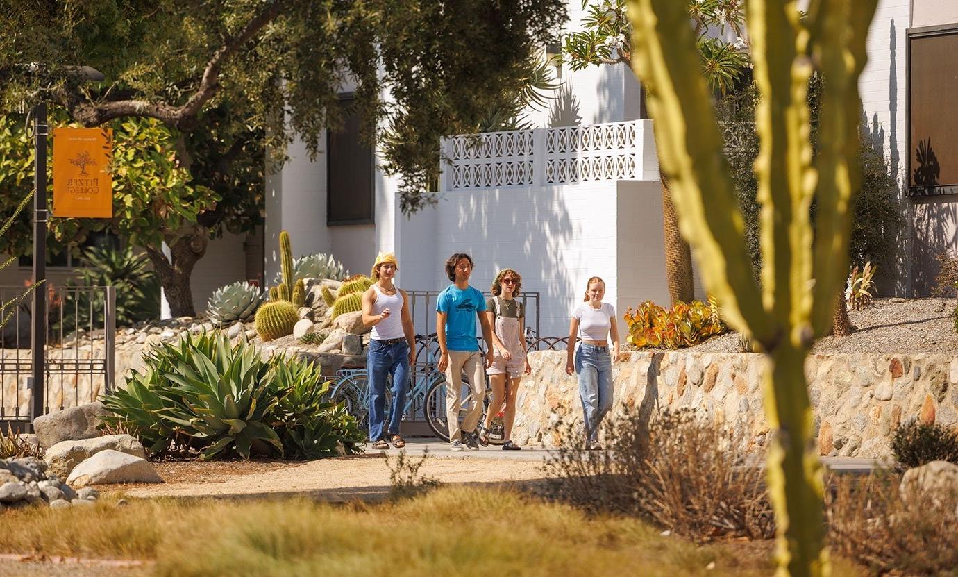 Four students walk on the pathway next to holden garden